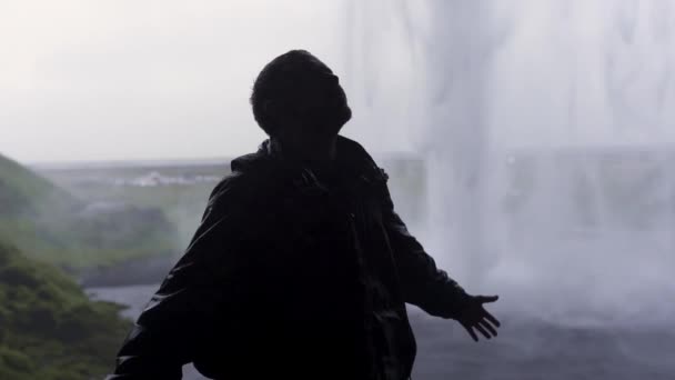 在冰岛的阴天里 背着背包的无忧无虑的男性探险家在塞尔贾拉下伸展着胳膊四处打转 并滑落在浮冰瀑布下 — 图库视频影像