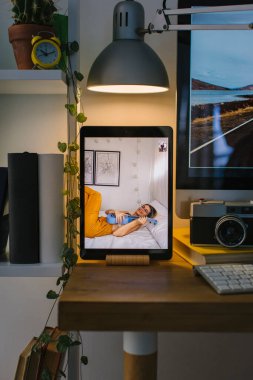 Corona Times 'daki bir arkadaşıyla video görüşmesi sırasında yatağında ukulele çalan bir kız. Tablet bir masanın üstünde, bir bilgisayar, birkaç kitap ve bir kamera ile birlikte..