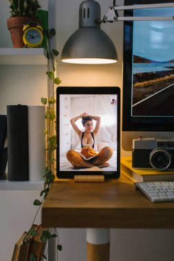 Corona Times 'daki bir video görüşmesi sırasında genç sarışın kız saçını topluyor. Tablet bir masanın üstünde, bir bilgisayar, birkaç kitap ve bir kamera ile birlikte..