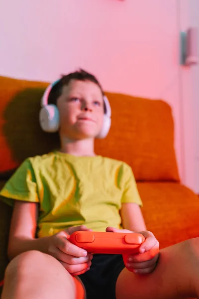 リビングルームのソファーでビデオゲームをプレイしながらゲームパッドでワイヤレスヘッドフォンに焦点を当てた少年 — ストック写真