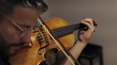 Gözlüklü yetişkin bir adam kendi luthiery atölyesinde çalışıyor ve stüdyoda ayakta dururken keman çalıyor.