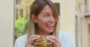 Hamburger yiyen genç mutlu kadın.