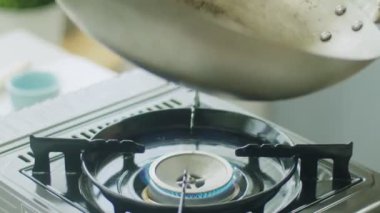 Yüksek açılı ağır çekimde, mutfakta gaz sobasında pişirirken, kimliği belirsiz bir kadının kızartma tavasını yağ ile kaplaması.