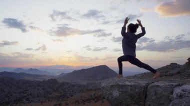 Gün batımında doğada yoga yaparken, bir dağın tepesinde çıplak ayaklı bir kadın duruşu.