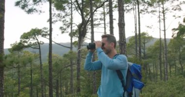Sırt çantalı, mutlu, olgun erkek turistin bakışları altında dürbünle etrafa bakarken yaz haftasonunu ormanda geçiririz.