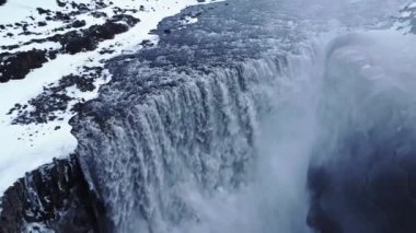 Soğuk kış gününde İzlanda 'nın doğasında, karlı uçurumdan düşen temiz şelalenin drone görüntüsünü büyüt