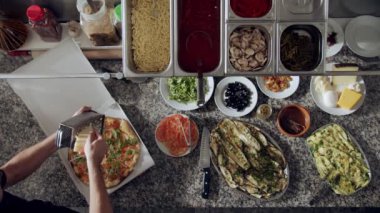 Yavaş çekimde, parmesan peyniri rendeleyen erkek pizza üreticisini karton bir pizzanın üzerine yatırıp mermer tezgahta çeşitli sebzelerin ve pizzacının mutfağındaki çatalların yanında servis için hazırlarken görüyoruz.