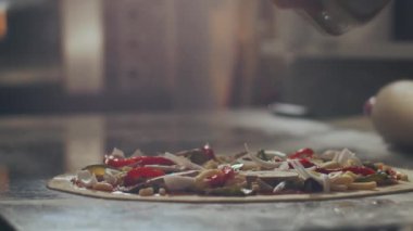 Restaurant mutfağında çalışırken tanınmayan bir erkek aşçı pişmemiş pizzayı pişirmeden önce cam çömlekten kurutulmuş keklik otu döküyor.