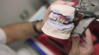 Laboratuvarda takma diş yaparken eklem makinesinde çenenin alçı kalıbını inceleyen isimsiz erkek diş teknisyeninin kırpma görünümü