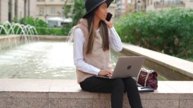 Telefon görüşmeleri sırasında binanın yanında elinde kahve ile netbook 'ta yazan yoğunlaşmış İspanyol kadın vücudu.