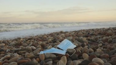 Günbatımında Stony Beach 'te deniz suyuyla yıkanan kirli tıbbi maskeler çevresel kirlilik kavramını gösteriyor.