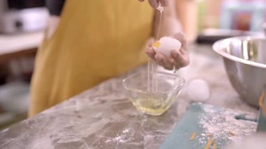 Evde yemek hazırlarken çiğ yumurta sarısını beyazdan ayıran tanınmamış orta yaşlı bir dişi.