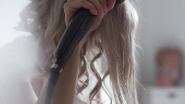 Side view of female with iron curling hair at home while making stylish hairdo