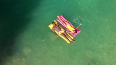 Yukarıdan bakıldığında çok ırklı erkek ve kadının yaz tatili boyunca temiz göl suyunda şişme şamandıralarda uzandıkları görülüyor.
