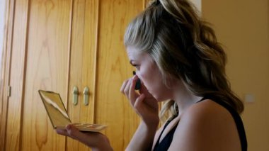 Renkli göz farı ve ayna ile palet tutan genç bir kadın ve evde güzellik prosedürü sırasında kirpiklerine siyah rimel sürüyor.