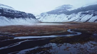 Soğuk kış gününde İzlanda 'da, karlı dağ sırasının yakınındaki vadideki nehir haliçlerinin manzaralı manzarası.