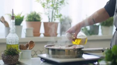 Gerçek zamanlı önlüklü anonim bir kadın. İtalyan ossobuco pişirirken cam şişeden tavaya kızgın et ekliyor.