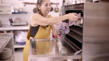 Orta yaşlı Meksikalı kadın aşçı evde mutfakta tatlı hazırlarken metal pişirme tepsisini fırından çıkarıyor.