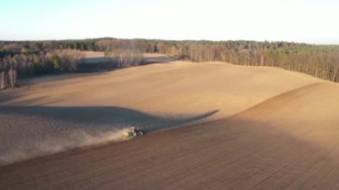 Gün batımında yemyeşil ağaçlarla çevrili tarımsal alanda traktörün sürüş görüntüsü.