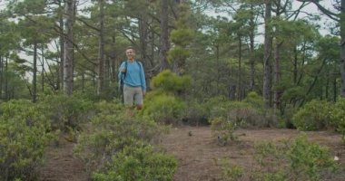 Sırt çantalı ve bastonlu yetişkin bir adamın gündüz vakti yeşil ağaçlıklarda yürüyüş yaparken fotoğrafını çekiyorum.