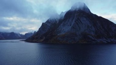 Norveç 'te sisli gökyüzünün altında karlı zirveleri olan devasa kayalık dağlarla çevrili muhteşem deniz manzarası.
