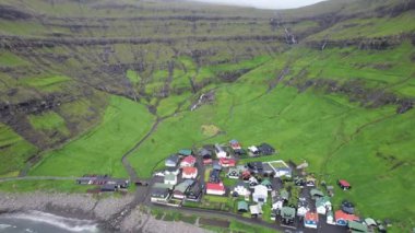 Faroe Adaları 'nda fırtınalı bir günde dalgalanan denizin yanındaki yeşil fiyortta küçük bir yerleşim yerinden.