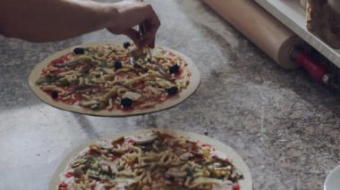 Pizza hazırlama işlemi mermer tezgahın üzerinde çeşitli sebzeler ve pizzacıdaki malzemelerle yapılıyor.