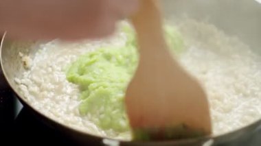 Aşçıbaşı mutfakta fırında yemek pişirirken tavada yeşil pesto sosuyla spatulayı karıştırıyor.