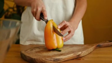 Mutfaktaki salata hazırlığı sırasında tahtadan kesme tahtasıyla taze olgun dolma biberi kesen tanınmamış kişi.