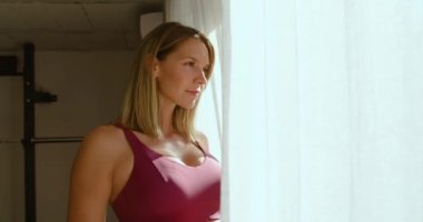 Eğitimden sonra evde panoramik pencereden dışarı bakarken şişeden su içen zayıf kadının yan görüntüsü