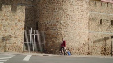 Kaldırımda yürüyen bir erkek turistin yan görüntüsü yaya geçidinin yanında eski bir binanın yanındaki tekerlekli bavuluyla.