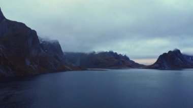Norveç 'te sisli gökyüzünün altında karlı zirveleri olan devasa kayalık dağlarla çevrili muhteşem deniz manzarası.