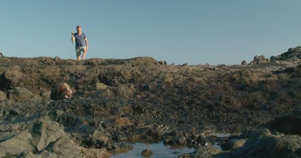 カジュアルな服で成熟した男性のショットを追跡し 海洋ジアザー近くの火山の海岸でスティックを歩いて テネリフェ島 カナリア諸島 スペインで成功を祝うために腕を上げます — ストック動画