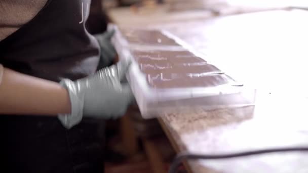 エプロンのクロップアノニマスチョコレートのハイアングルサイドビューと日中の菓子の作業中に金型の液体チョコレートを形成する手袋 — ストック動画