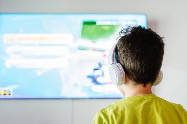 Kablosuz kulaklıklı, açık salonda TV 'de ilginç video oyunları oynayan isimsiz bir çocuğun arka planı.