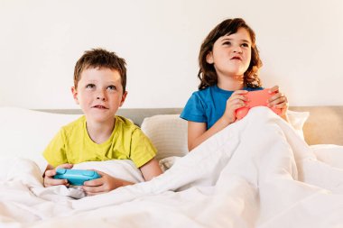 Evde yatak odasındaki battaniyenin altında birlikte rahat bir yatakta otururken oyun kağıtlarıyla oyun oynayan odaklanmış kardeşler.