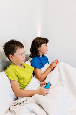 Evde yatak odasındaki battaniyenin altında birlikte rahat bir yatakta otururken oyun kağıtlarıyla oyun oynayan odaklanmış kardeşlerin yan görünüşü