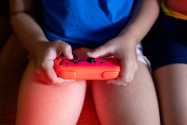 Oyun kağıtlarıyla tanınmayan kardeşler oturma odasında loş ışıkla otururken video oyunu oynuyorlar.