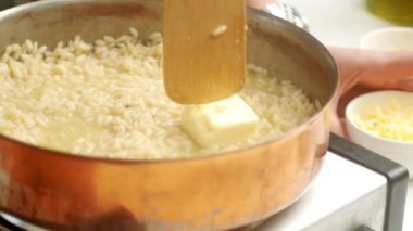 Anonim şef mutfakta risotto pişirirken tavaya tereyağı ve rendelenmiş peynir ekliyor.