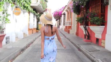 Yazlık kıyafetli şık bir kadın renkli bir binanın yanında yürüyor.