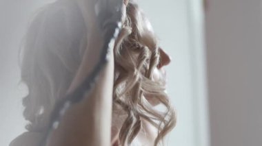 Side view of female with iron curling hair at home while making stylish hairdo