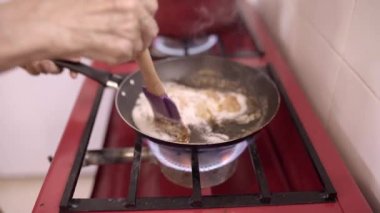 İsimsiz olgun kadın aşçı sıcak tavada malzemeleri karıştırırken ev mutfağında ocakta kahveyle tatlı hazırlıyor.