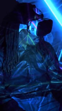 Siyah gözlüklü Afro-Amerikan erkek, karanlık odada renkli neon ışıklar altında siber uzayı keşfederken etrafı kolaçan ediyor.