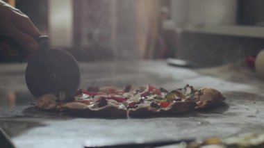 Anonim pizza üreticisi restoran mutfağında çalışırken taze pişmiş iştah açıcı sıcak pizzayı mermer tezgahta kesiyor.