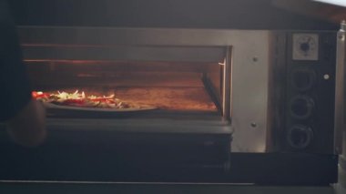 Metal kürekli isimsiz bir aşçı geleneksel İtalyan çiğ pizzasını mermer masa üstünden restoran mutfağında pişirmek için fırına götürüyor.