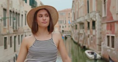 Çizgili bluz ve hasır şapkalı genç bir kadın Venedik, İtalya 'da hafta sonu gondollarıyla köprü kenarına yaslanıyor.
