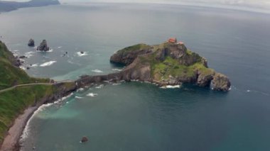 Drone view of paving stone way leading along stone bridge and ridge of rocky hill to lonely house on island Gaztelugatxe surrounded by tranquil sea water under cloudy sky in Basque Country