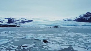 İzlanda 'nın bulutlu bir gününde Vatnajokull Ulusal Parkı' nın volkanik arazisinde karlı dağlarla çevrili denizde yüzen buz parçalarının manzarası.