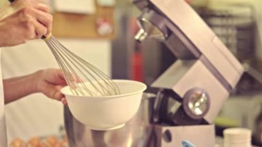 Restaurant mutfağında hamur işi yaparken çırpıcıyla karıştırdığı malzemelerle tanınmayan profesyonel kadın pasta şefinin kırpılmış yan görüntüsü.