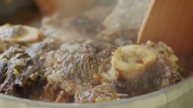 Gerçek zamanlı tahtadan spatulaları olan, mutfaktaki elektrikli ocakta, paslanmaz tavada ossobuco pişiren isimsiz bir insan.